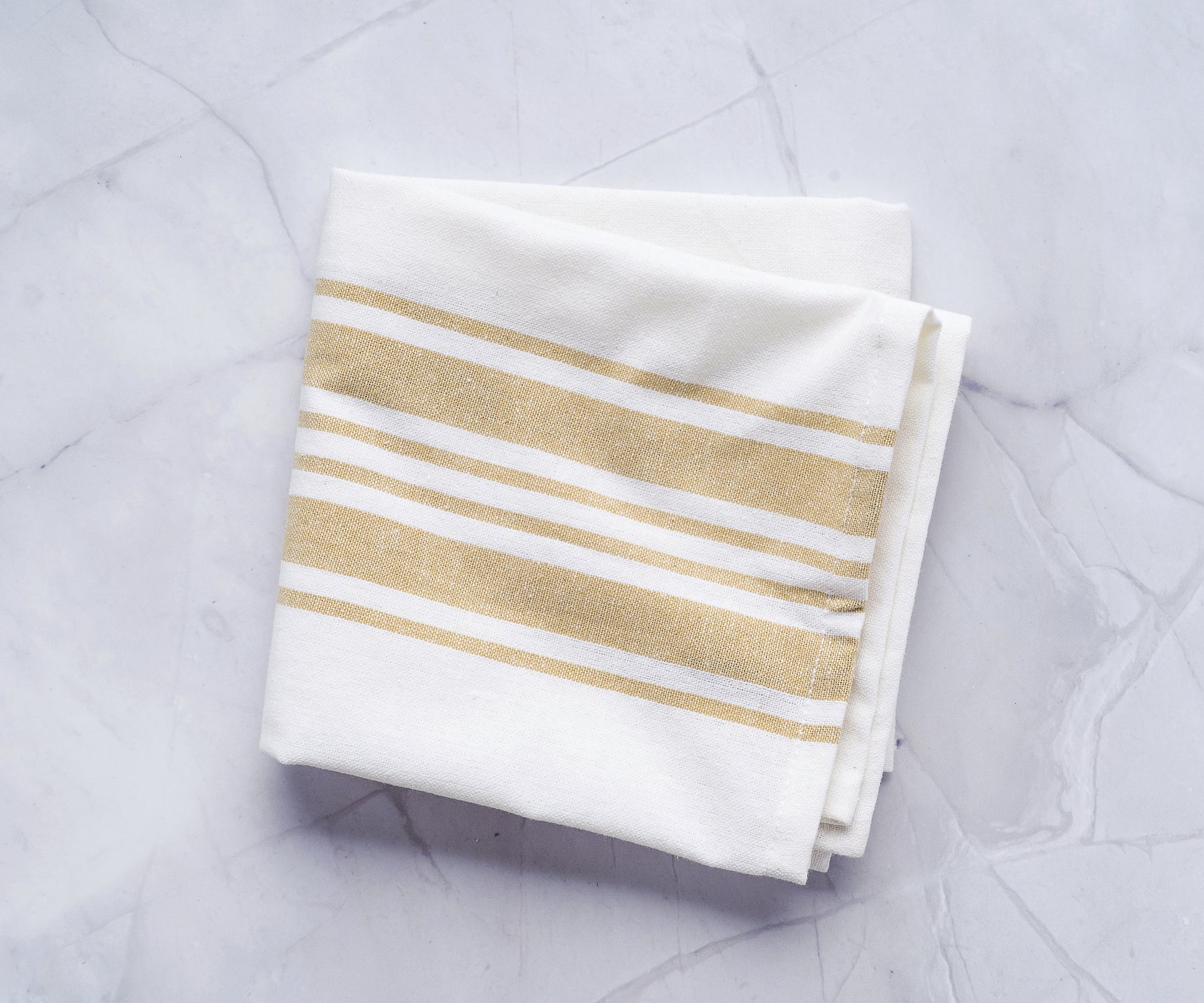 Close-up of a white kitchen towel with gold stripes on a polished marble countertop