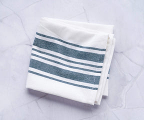Single kitchen towel with blue and white stripes lying on a marble countertop