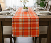 Orange-red tartan plaid cotton table runner with white, black, and yellow checks adding a vibrant festive touch to a Christmas dining table.
