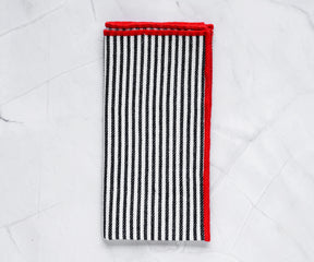 Black cotton napkins with red borders styled on a rustic wooden dining table for a cozy farmhouse look.