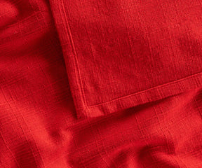 Red rectangular cotton tablecloth spread over an outdoor picnic table, creating a vibrant and classic look for garden parties or outdoor dining.