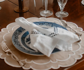 Beige scalloped cotton placemats with white accents on a round dining table.