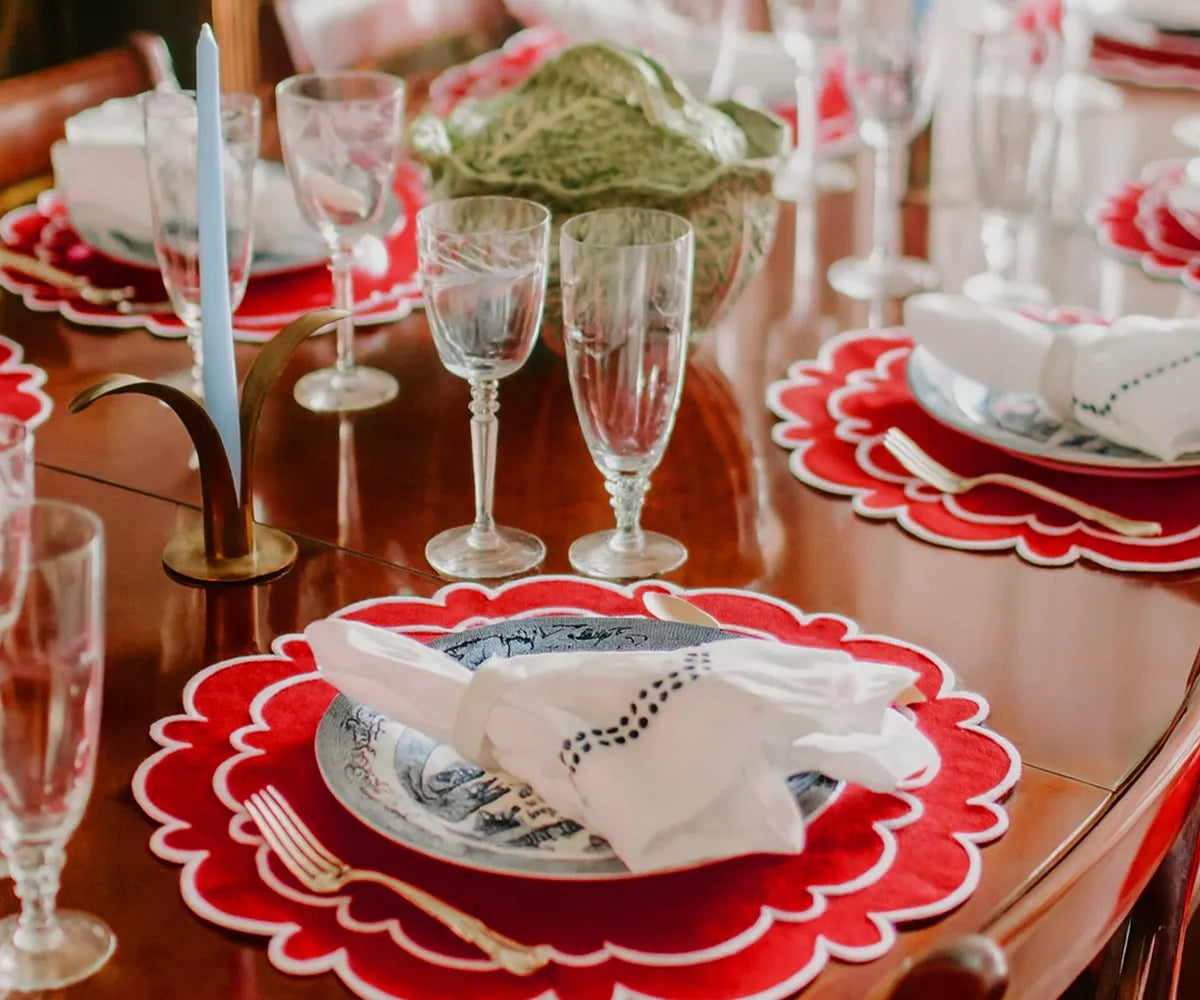 Red scalloped cotton placemats with white accents on a round dining table.