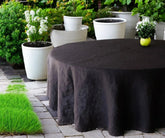 A black linen round tablecloth on a table outdoors, with chairs around it and plants in the background.