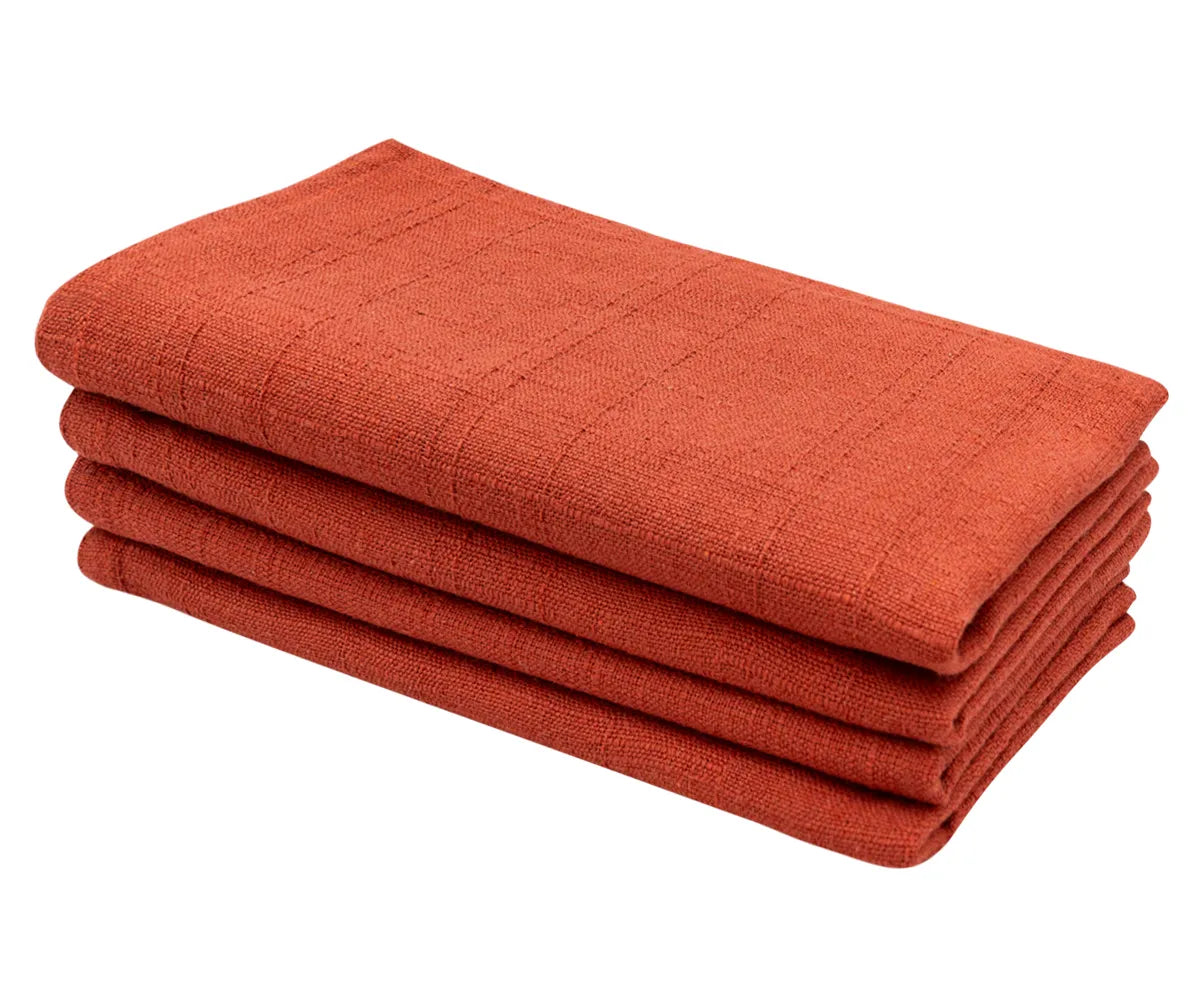 Rustic rust color cotton dinner napkin neatly folded on an elegant holiday dining table with festive tableware