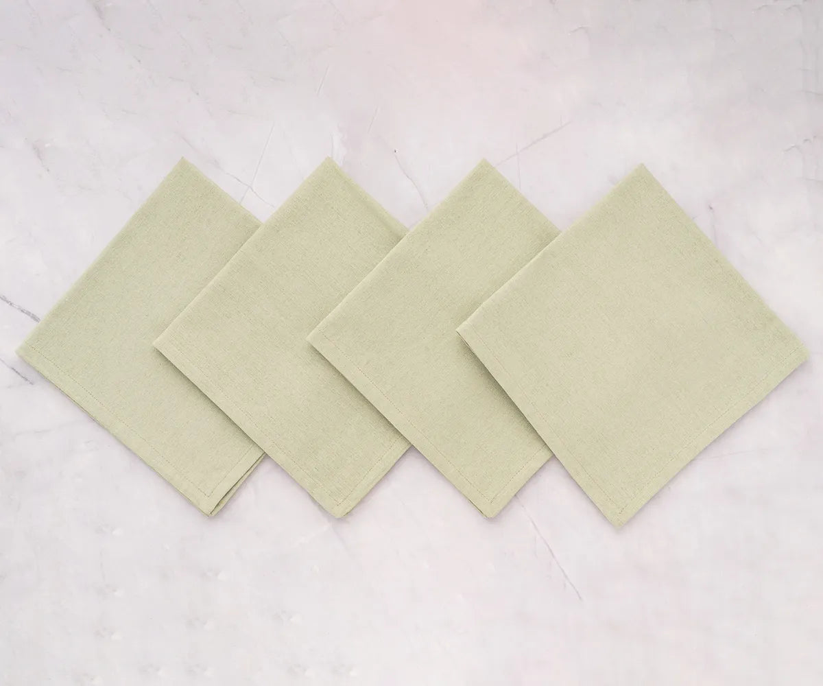 Elegant sage green cotton dinner napkin neatly folded on a rustic dining table with striped tablecloth and classic dinnerware