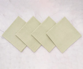 Elegant sage green cotton dinner napkin neatly folded on a rustic dining table with striped tablecloth and classic dinnerware