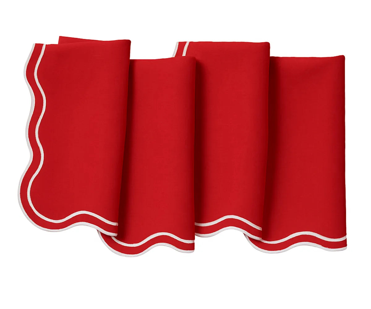 Folded red scalloped cotton napkins on a wooden dining table, ready for a festive meal.