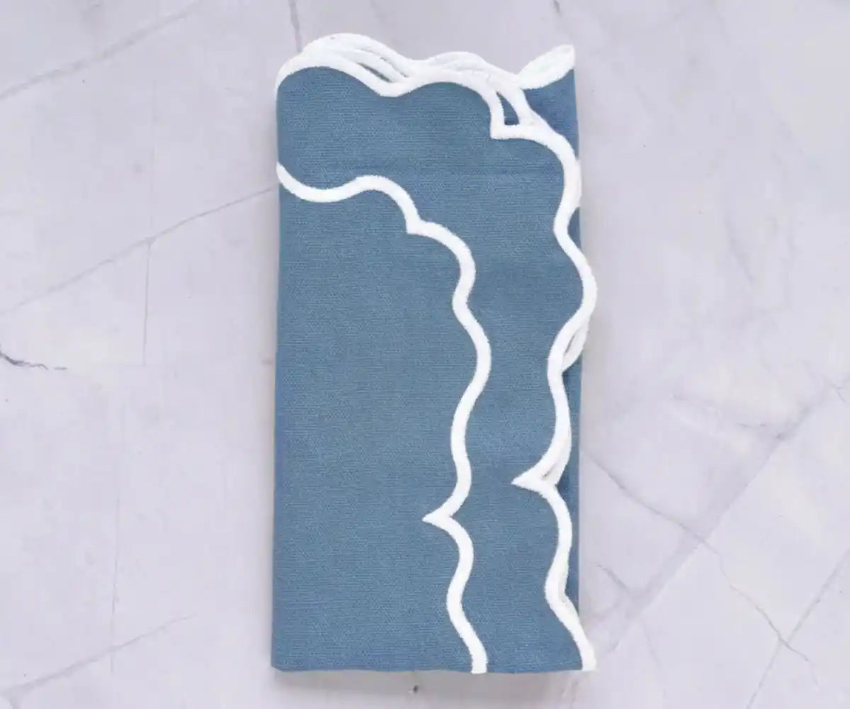 Dusty blue cotton napkins with white scalloped border neatly folded for table setting