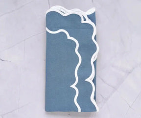 Dusty blue cotton napkins with white scalloped border neatly folded for table setting