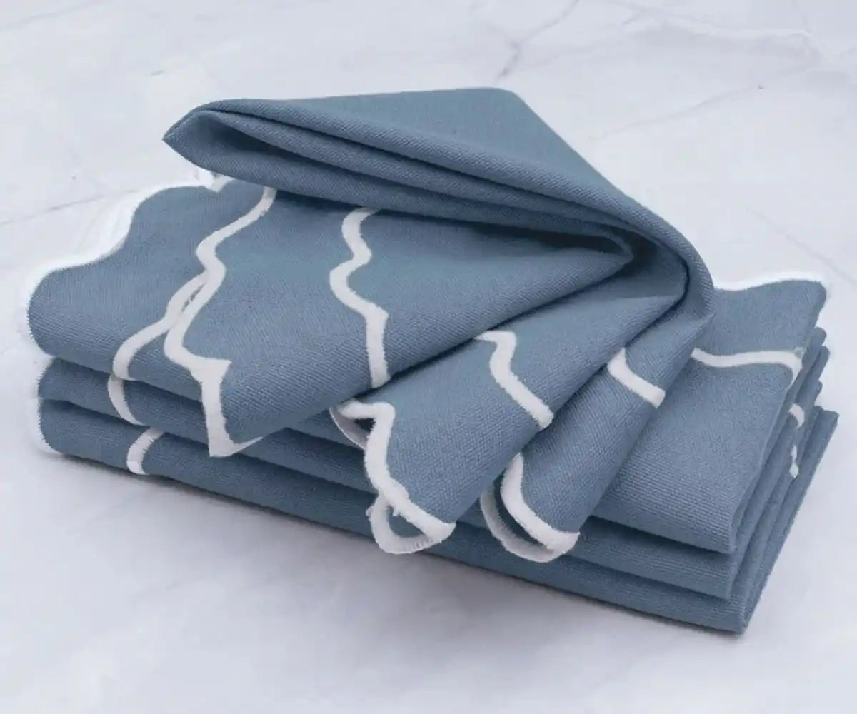 Dusty blue cotton napkins with white scalloped border neatly folded for table setting