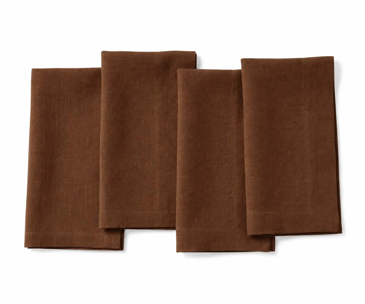Set of four coffee brown signature linen napkins neatly folded side by side on a white background