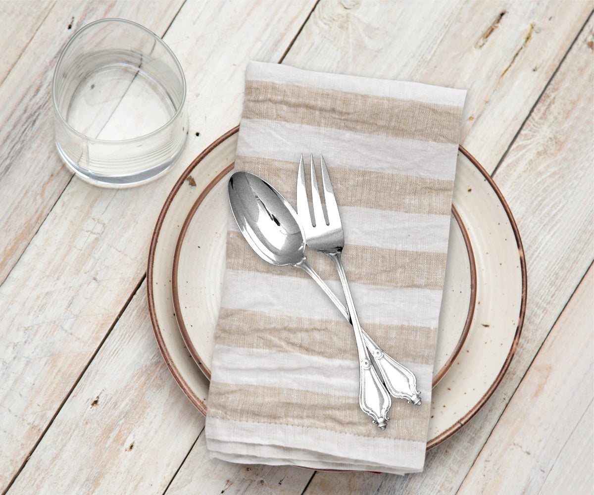 Silver spoon and fork on a striped napkin with a glass of water on a wooden table.