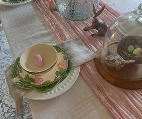 Easter-themed table setting with decorative plates, a teacup, and a cloche with eggs.