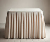 Fabric table skirt in soft beige cotton covering a party table with decorative pleats