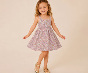 Toddler girl wearing a sleeveless pink floral cotton toddler dress, posing against a beige background in a comfortable summer outfit.
