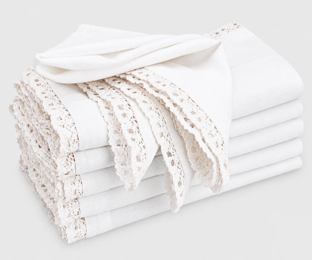 A stack of folded white cotton cloth napkins featuring decorative lace trim and scalloped edges