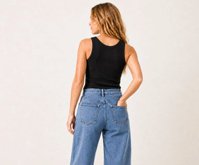 A woman shown from the back wearing a black ribbed tank top and high-waisted light blue wide-leg jeans, standing against a plain off-white studio background.