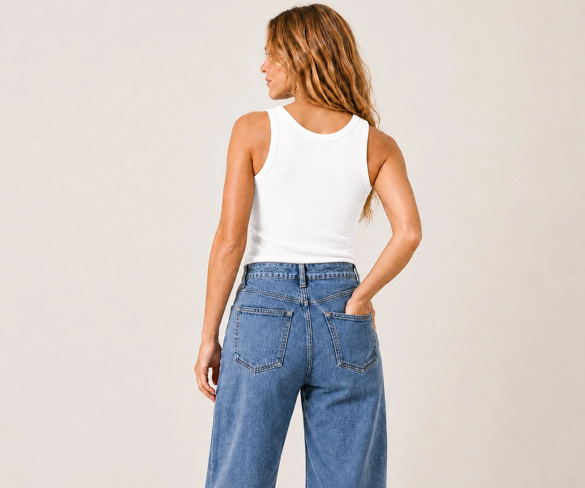 A woman shown from the back wearing a white ribbed tank top and high-waisted blue wide-leg jeans, standing against a plain light beige studio background.