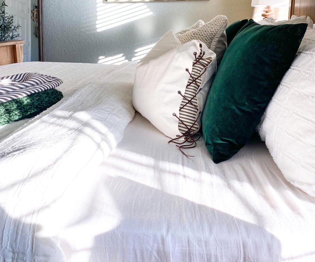 Bed dressed with white cotton fitted sheets and green pillows