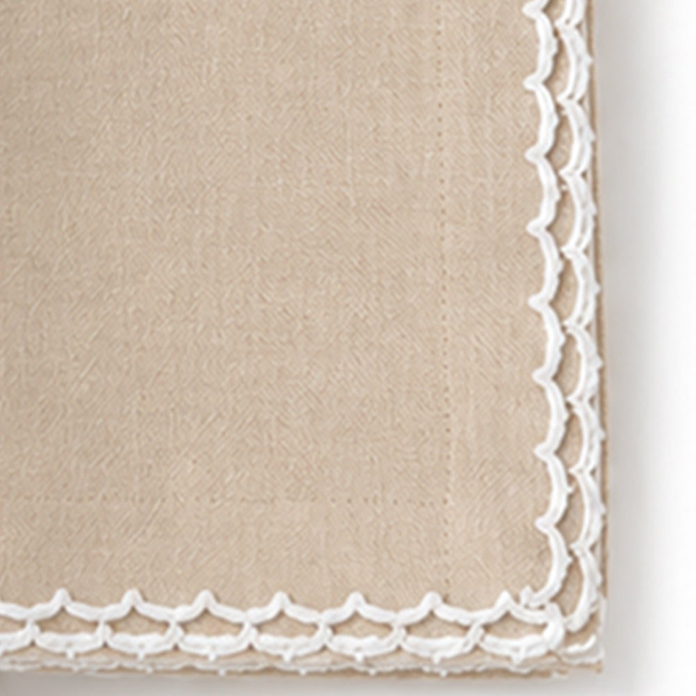 Close-up of a beige cotton napkin featuring a white scalloped embroidered edge.