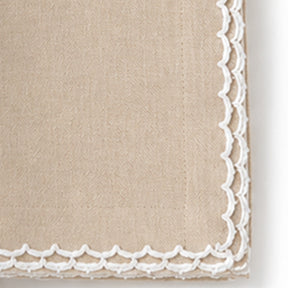 Close-up of a beige cotton napkin featuring a white scalloped embroidered edge.