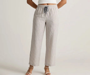 Front view of a model wearing high-waisted beige wide-leg cotton linen trousers with thin vertical pinstripes, featuring a dark blue drawstring and paired with white strappy sandals.