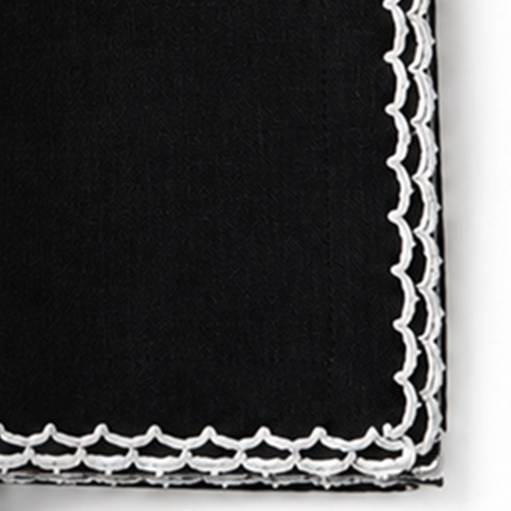 A close-up of a black fabric napkin with a white scalloped embroidered border.