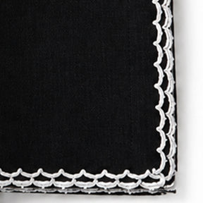 A close-up of a black fabric napkin with a white scalloped embroidered border.