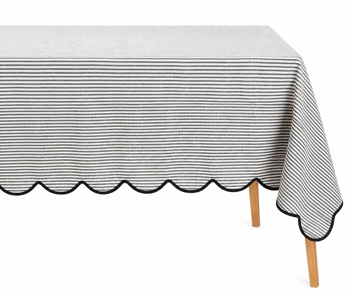 Black and white thin striped linen tablecloth with a decorative black scalloped edge draped over a table.
