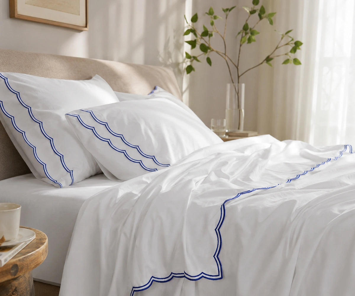 White bed sheet set with blue scalloped embroidery on the pillowcases and flat sheet.