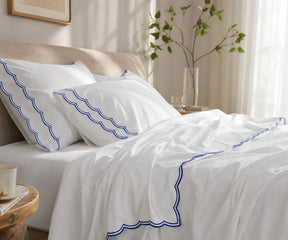 White bed sheet set with blue scalloped embroidery on the pillowcases and flat sheet.
