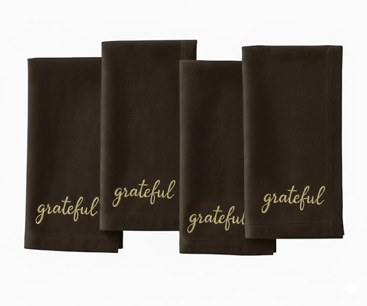 Brown cloth napkin with beige “Grateful” embroidered lettering for rustic table settings.