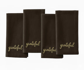 Brown cloth napkin with beige “Grateful” embroidered lettering for rustic table settings.