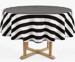 A round table covered with a black and white striped tablecloth, shown on a light wood table against a plain white background.