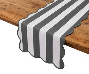Charcoal grey and white cabana striped table runner with scalloped edges on a rustic wood dining table.