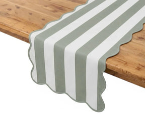 Sage green and white cabana striped table runner with scalloped edge detail placed on a wooden table.