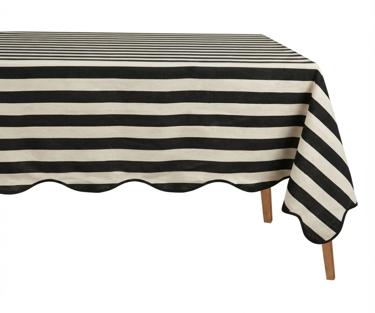 Black and white cabana striped tablecloth with a scalloped edge on a wooden table.