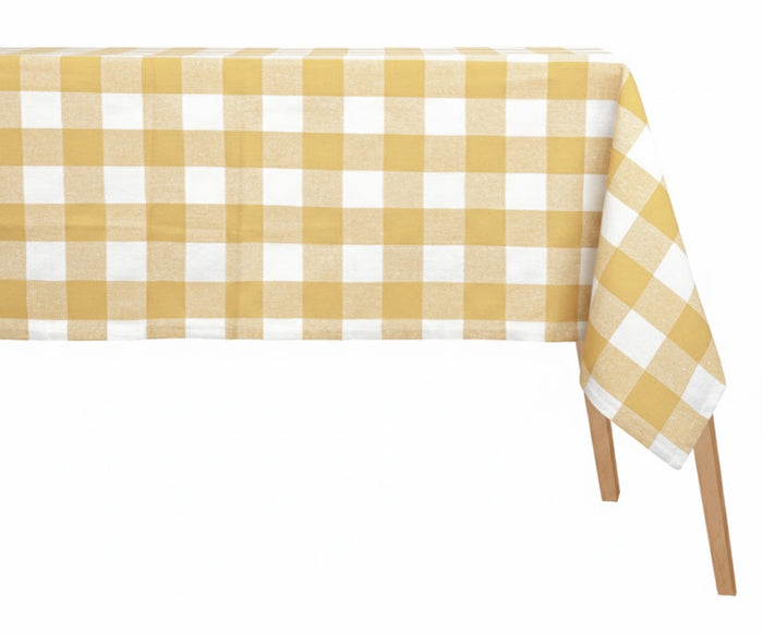 Pale yellow and white checkered cotton tablecloth in classic gingham plaid pattern on rectangular dining table