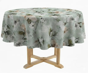 Round linen tablecloth with botanical leaf pattern draped over a wooden pedestal table, displayed in a clean studio setting with natural fabric folds.