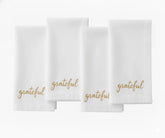White cotton napkin with “Grateful” embroidered in beige thread for holiday table décor.