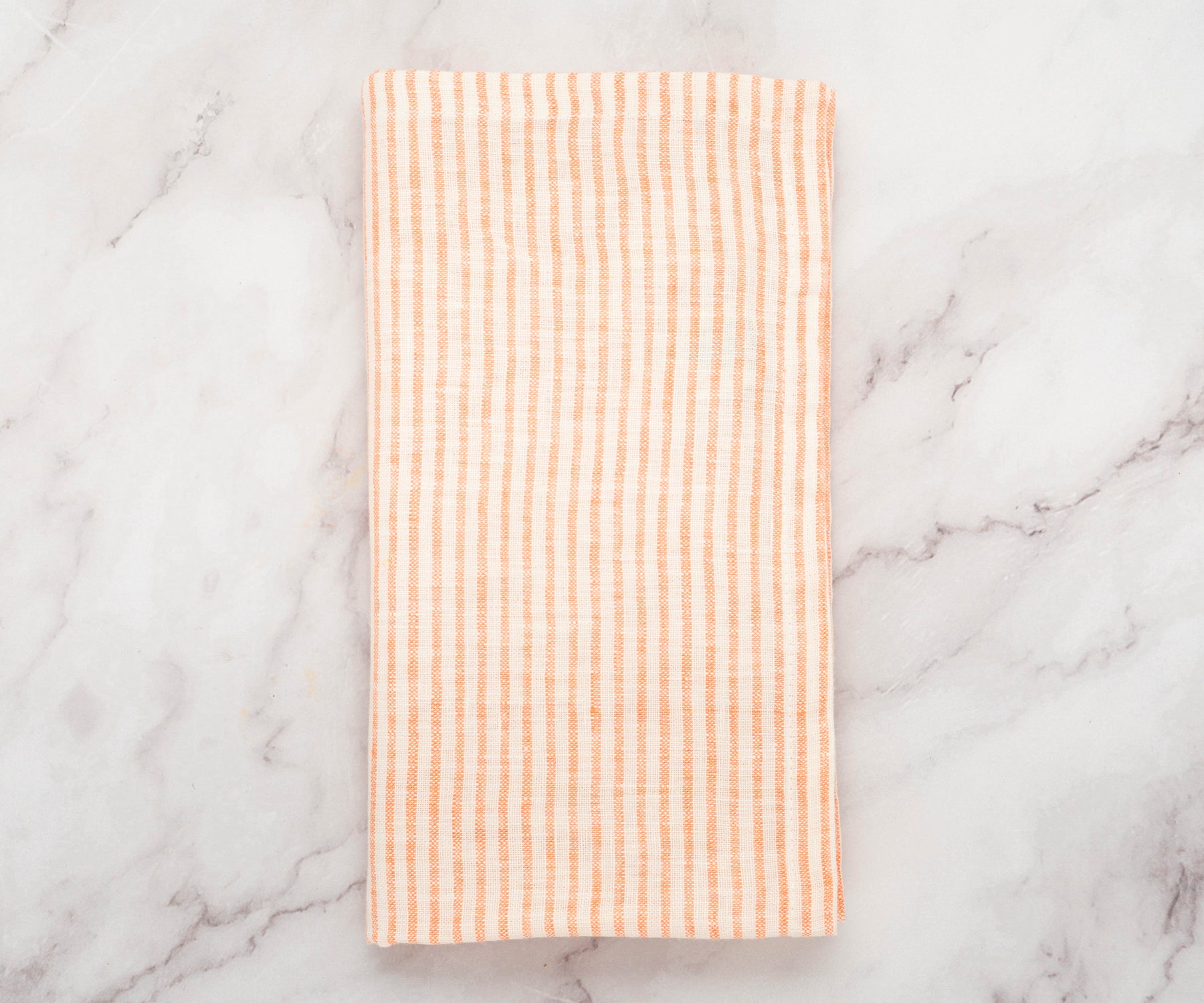 Stack of orange linen napkins with white stripes neatly folded on a wooden table