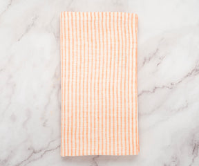 Stack of orange linen napkins with white stripes neatly folded on a wooden table
