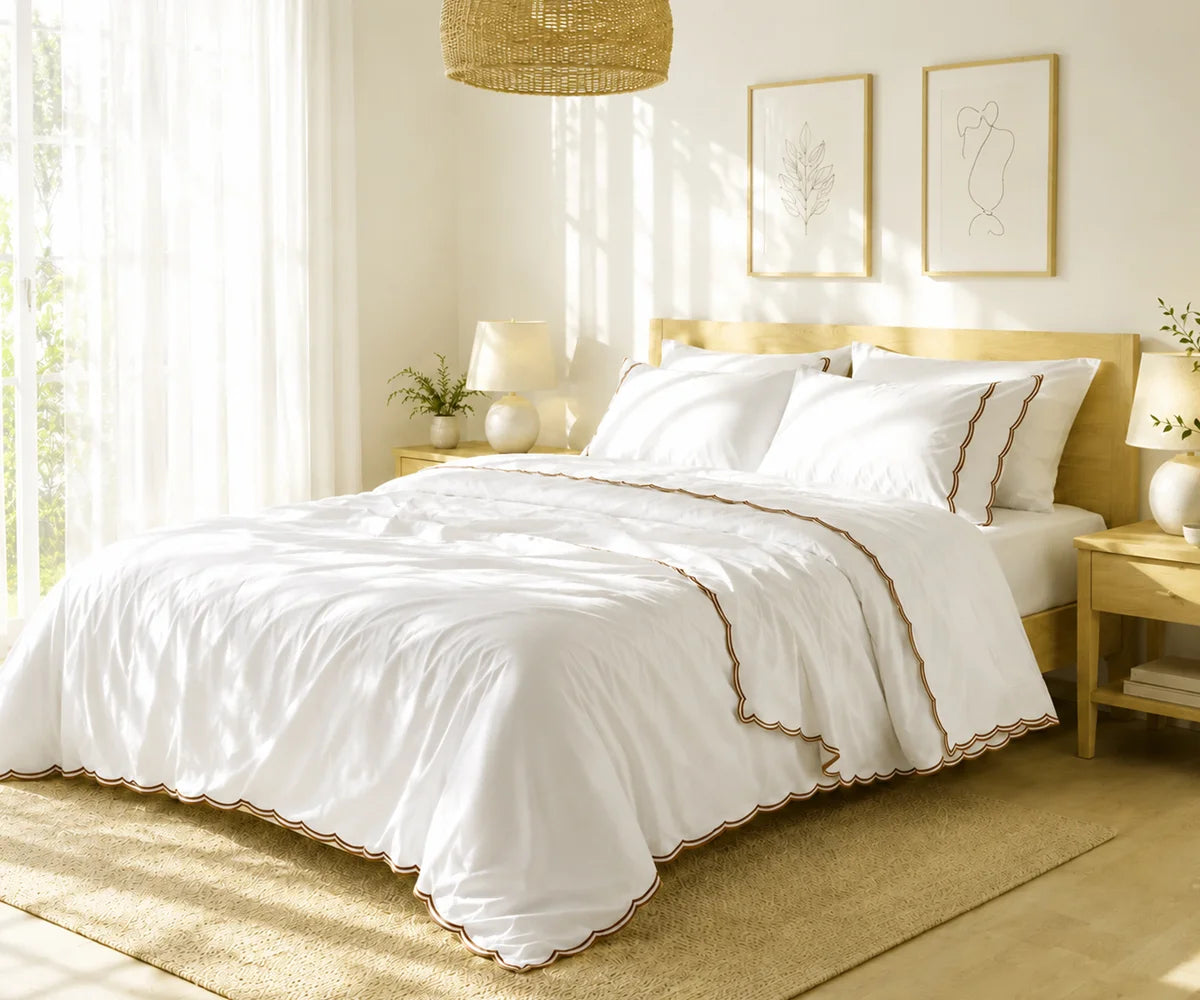 White scalloped bedspread with coffee brown trim styled on a bed in a sunlit modern bedroom