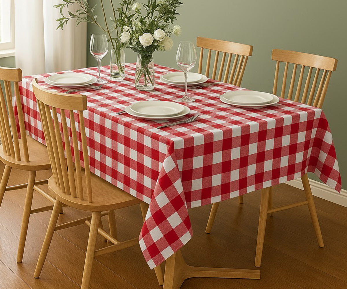Dining table set with a red and white checkered tablecloth, plates, glasses, and a vase of flowers.