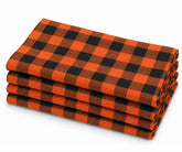 Folded stack of orange and black buffalo plaid cotton dinner napkins against a white background.