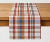 Rust, cream and blue cotton plaid table runner displayed across a wooden dining table, creating a warm autumn and Thanksgiving table setting.