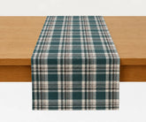Deep teal plaid table runner with cream and dark brown stripes draped over a wooden dining table.