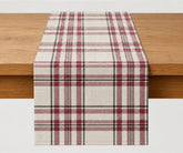 Burgundy tartan table runner in cream, muted red, and black plaid cotton, styled on a wooden dining table for Christmas and holiday table decor.
