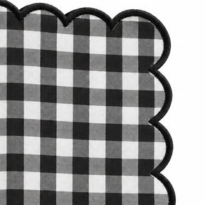 Close-up of black and white gingham cotton dinner napkin with dark green scalloped embroidered edge.